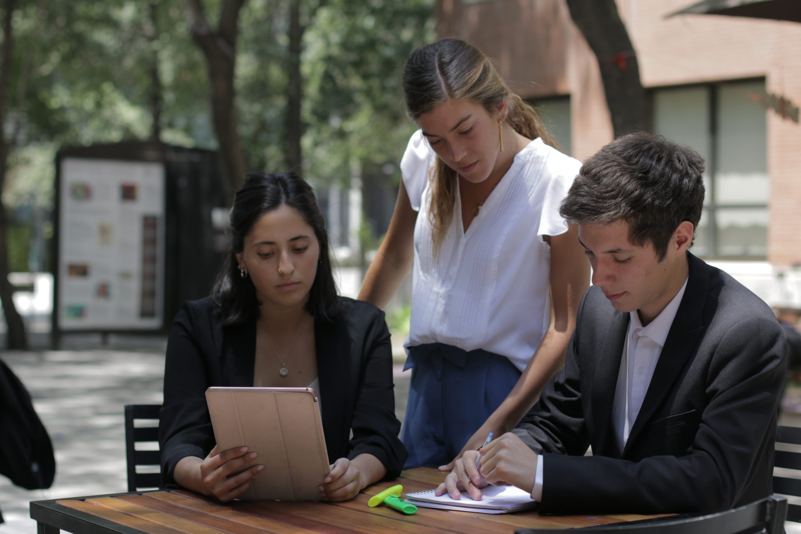 Estudiantes en el patio estudiando con un cuaderno y una tablet.