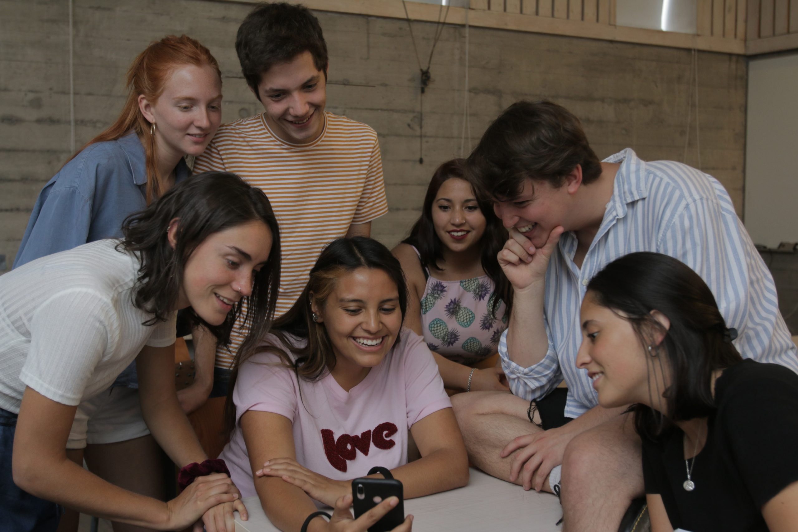Estudiantes reunidos viendo algo en el celular y sonriendo.