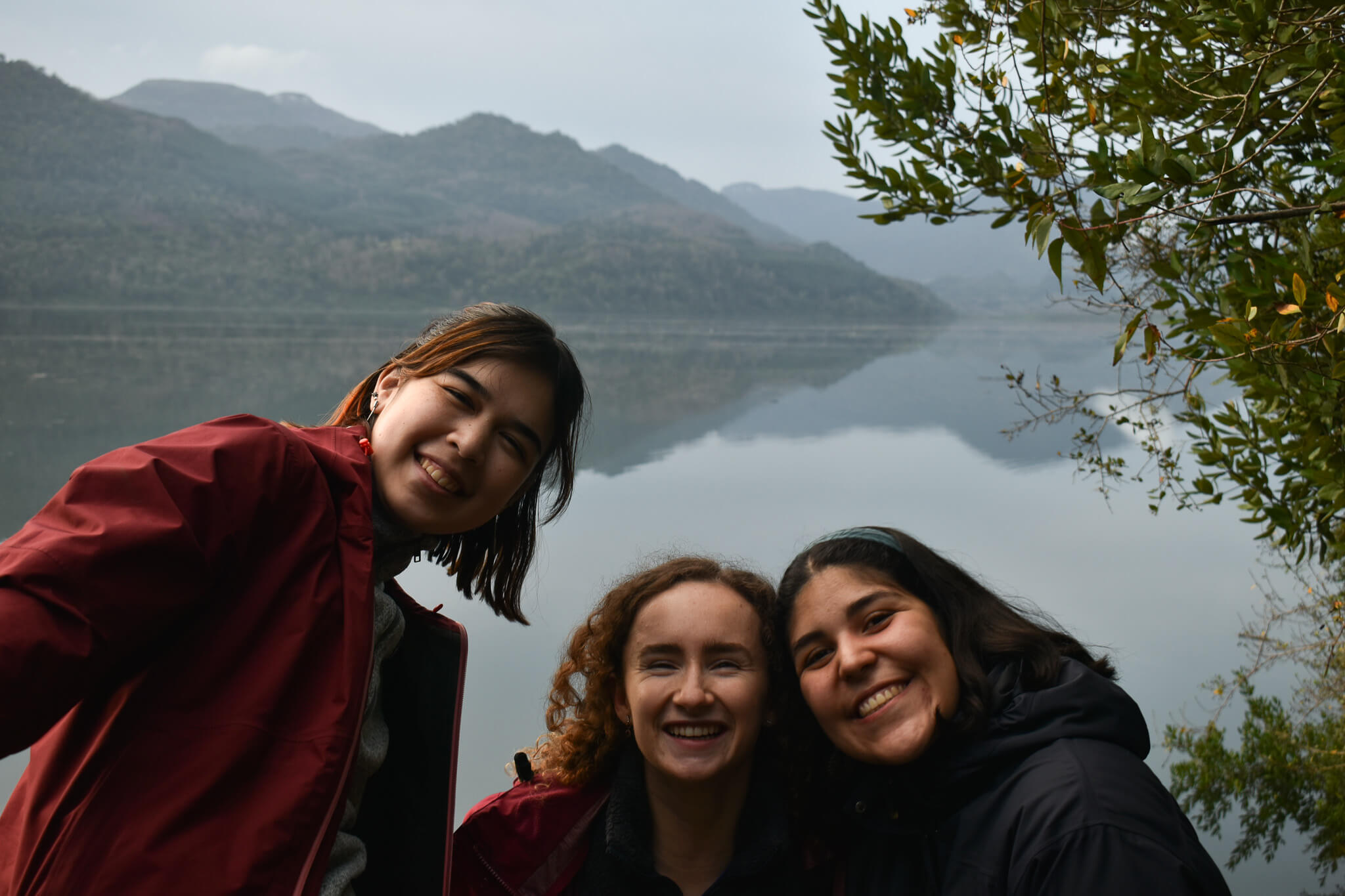 Tres chicas sonriendo frente a un lago en el sur.