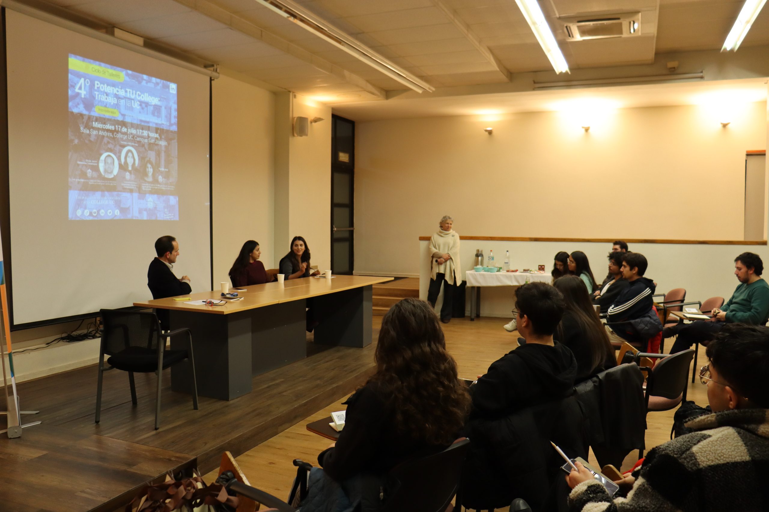Expositores del taller sentados en una mesa y estudiantes frente a ellos poniendo atención.